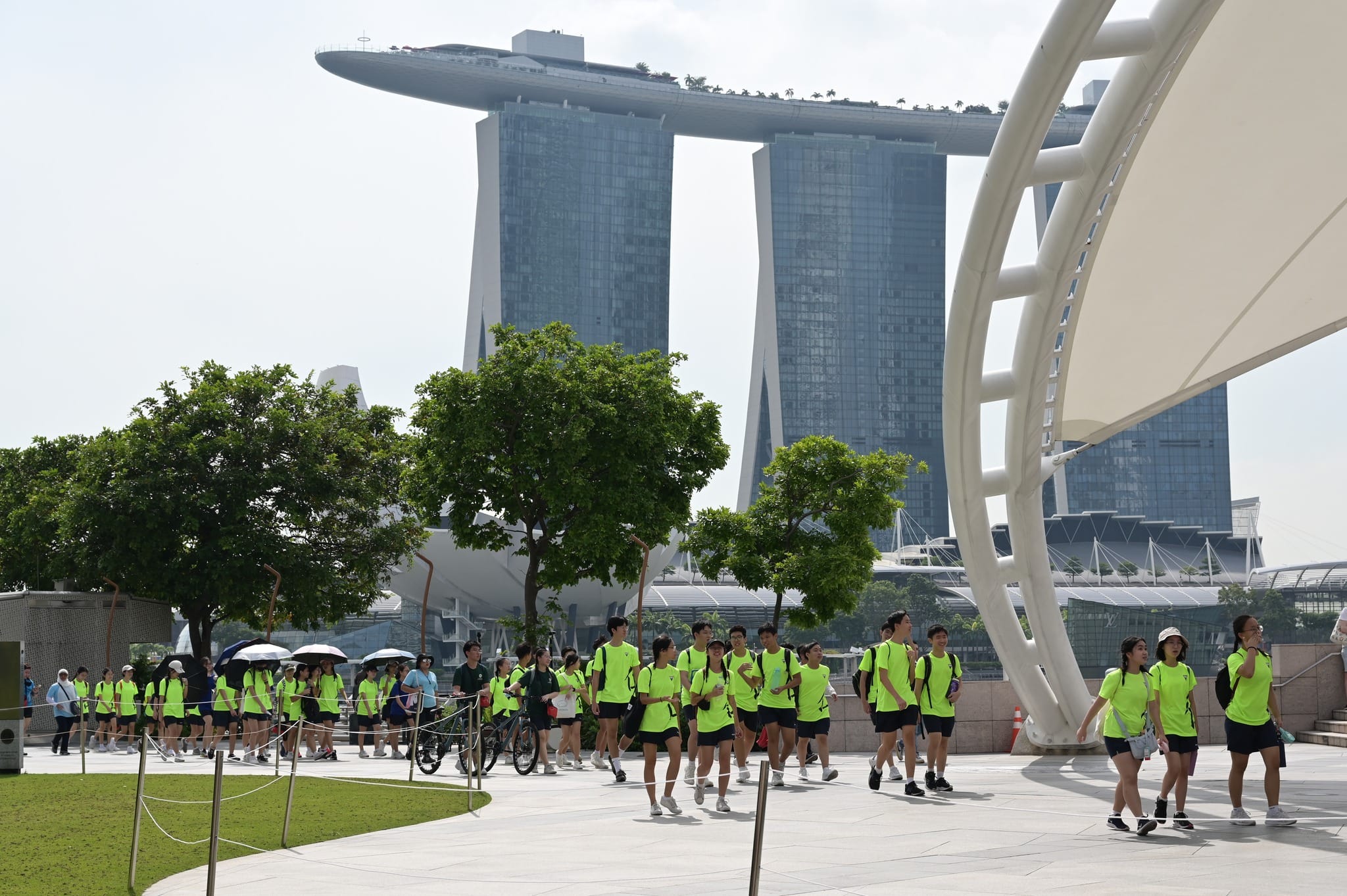 A large group in neon green uniforms walks along a plaza in front of Marina Bay Sands hotel in Singapore.